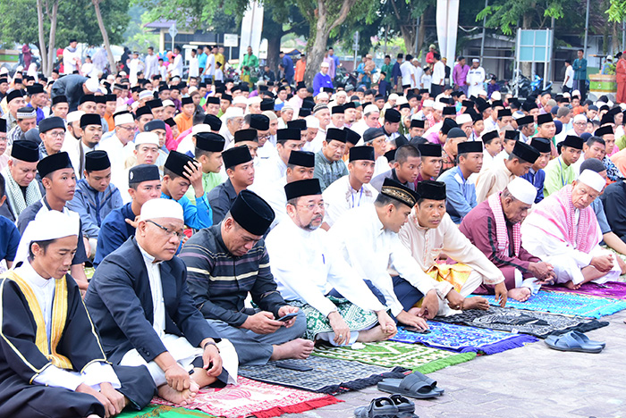Jamaah Muslim mengikuti salat Idul Fitri berjamaah di area terbuka dengan mengenakan pakaian muslim dan peci.