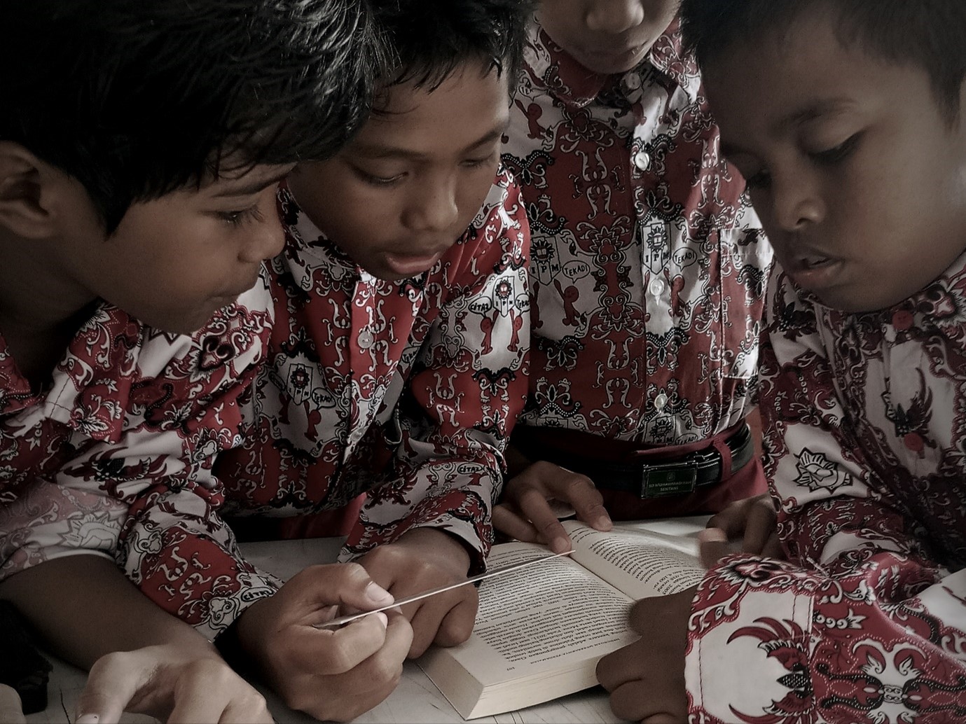 Empat siswa SD Muhammadiyah Sentani, mengenakan seragam batik merah khas, duduk mengelilingi sebuah meja dan fokus membaca sebuah buku bersama-sama.