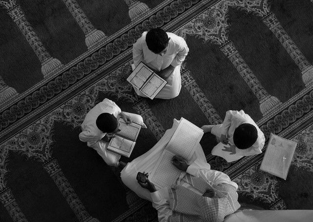 Foto hitam putih sekelompok orang sedang duduk melingkar di dalam masjid sambil membaca dan mendiskusikan Al-Qur’an sebagai ilustrasi kajian tafsir Islam.