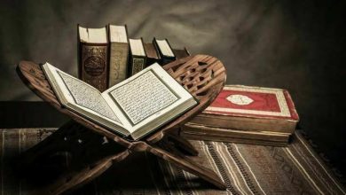 Al-Qur’an terbuka di atas rehal kayu dengan beberapa mushaf di latar belakang