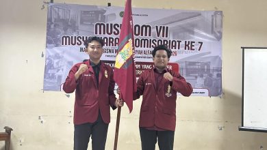 Dua kader PK IMM Al-Fatih FTIK UMPP berpose mengenakan jas merah IMM sambil memegang bendera organisasi dalam acara Musykom VII di Pekalongan.