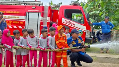 Petugas pemadam kebakaran Banyumas membimbing siswa TK Abas Two memegang selang air dalam simulasi edukasi pemadam kebakaran di depan mobil damkar merah.