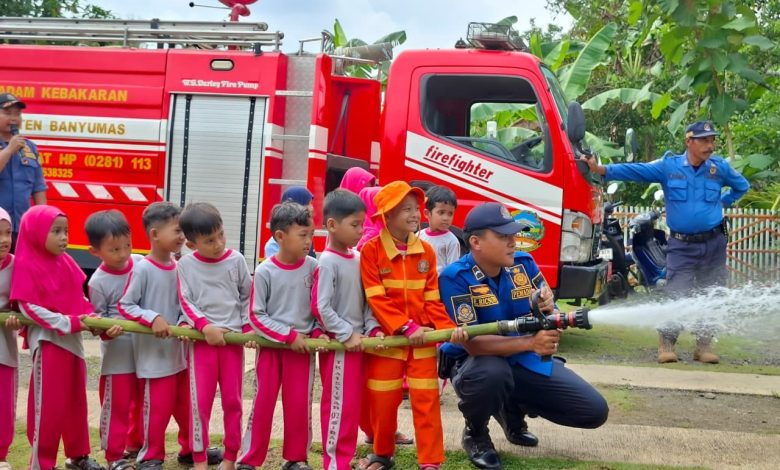 Petugas pemadam kebakaran Banyumas membimbing siswa TK Abas Two memegang selang air dalam simulasi edukasi pemadam kebakaran di depan mobil damkar merah.