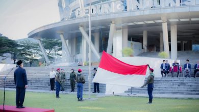 Pimpinan Universitas Muhammadiyah Surakarta (UMS), Prof. Dr. Harun Joko Prayitno, M.Hum., berdiri di mimbar inspektur upacara sambil mengamati petugas pengibar bendera merah putih yang sedang membentangkan bendera besar di halaman Gedung Induk Siti Walidah saat upacara peringatan Hari Pendidikan Nasional 2026. Peserta upacara dan pejabat lainnya duduk di bangku-bangku di latar belakang.