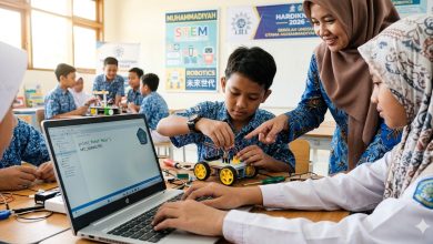 Dua pasang tangan siswa sekolah dasar sedang memegang obeng dan komponen elektronik kecil, merakit robot edukasi. Di sebelah mereka terdapat laptop yang menampilkan layar dengan blok-blok pemrograman berwarna. Latar belakangnya buram, menunjukkan ruang kelas yang terang.