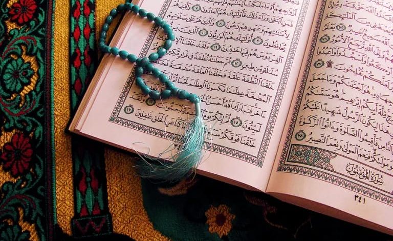 Mushaf Al-Qur'an terbuka di atas sajadah dengan tasbih berwarna biru, melambangkan kedalaman perenungan dan tadabbur ayat suci di tengah arus digital.