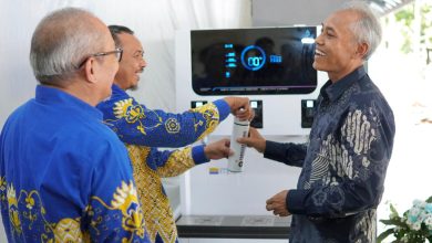 Ketua PK IMM Averroes FT UMS, yang mengenakan kemeja batik biru dengan motif kuning, sedang menerima kartu voucer untuk mengakses fasilitas Water Station dari Dekan Fakultas Teknik UMS, Prof. Ir. Mochamad Solikin, S.T., M.T., Ph.D. Dua pejabat lainnya menyaksikan proses penyerahan kartu voucer tersebut sambil tersenyum di depan mesin Water Station yang modern.
