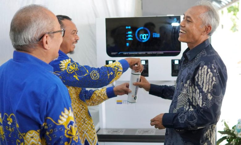 Ketua PK IMM Averroes FT UMS, yang mengenakan kemeja batik biru dengan motif kuning, sedang menerima kartu voucer untuk mengakses fasilitas Water Station dari Dekan Fakultas Teknik UMS, Prof. Ir. Mochamad Solikin, S.T., M.T., Ph.D. Dua pejabat lainnya menyaksikan proses penyerahan kartu voucer tersebut sambil tersenyum di depan mesin Water Station yang modern.