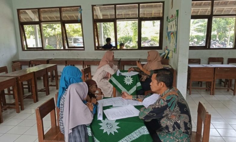 Suasana asesmen calon murid baru di MI Muhammadiyah Purwodadi. Seorang guru pria (kanan) mewawancarai orang tua di meja dengan taplak hijau berlogo Muhammadiyah, sementara dua calon siswa menunggu antrean di sebelah kiri. Di latar belakang, dua guru wanita juga melakukan sesi wawancara.