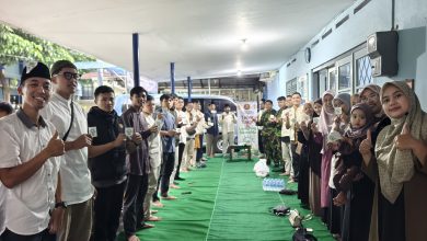 Anggota Pemuda Muhammadiyah Kota Magelang, laki-laki di kiri dan perempuan di kanan, berpose bersama di lorong dengan karpet hijau saat peluncuran komunitas motor Bikersmu. Mereka tersenyum ke arah kamera sambil mengacungkan stiker identitas Bikersmu sebagai simbol dakwah komunitas. Di latar belakang terdapat spanduk acara bertuliskan 'Melaunching Bikersmu Kota Magelang' dengan visual motor dan gedung PDM