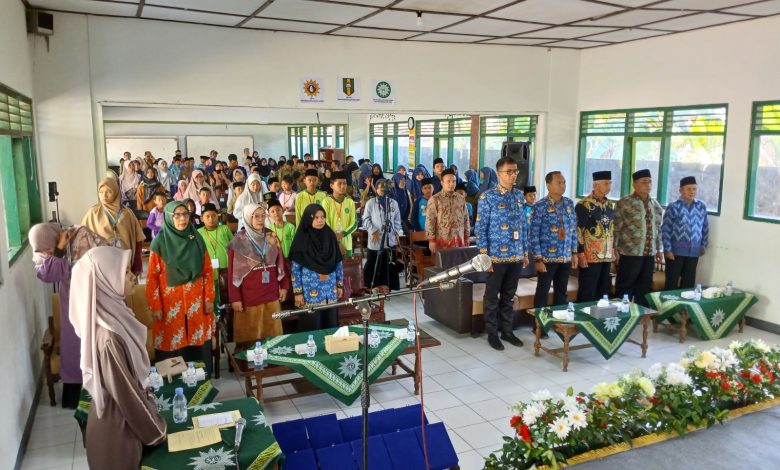 Suasana pembukaan Festival Sains dan Al-Qur’an SMP Muhammadiyah Jono di aula Komplek Pondok Pesantren Darul Arqom Muhammadiyah Bayan. Gambar menunjukkan barisan depan tamu undangan, termasuk Pimpinan Muhammadiyah dan perwakilan Dinas Pendidikan, berdiri di depan ratusan siswa SD/MI yang menjadi peserta. Aula terang, dengan dekorasi panggung bunga di latar depan dan beberapa spanduk kecil organisasi Muhammadiyah di dinding.