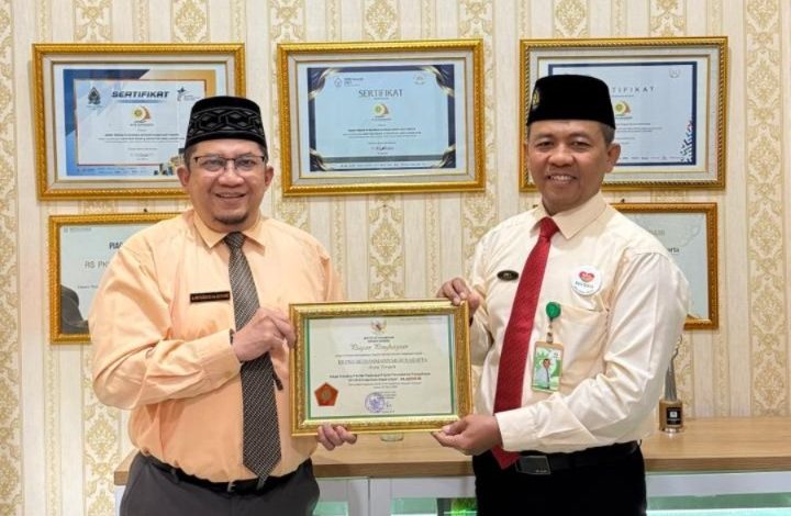 Dua pria berpeci menunjukkan piagam penghargaan Platinum P2HIV/AIDS dari Menteri Ketenagakerjaan RI untuk RS PKU Muhammadiyah Surakarta.