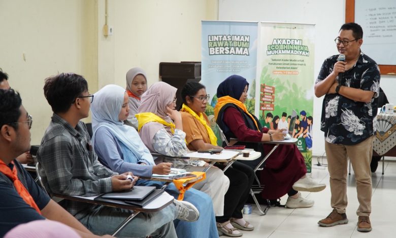 Peserta muda lintas iman sedang mendengarkan materi dalam pelatihan Akademi Eco Bhinneka Muhammadiyah yang disampaikan oleh seorang pemateri pria berbaju batik. Dua banner program terlihat di latar belakang.