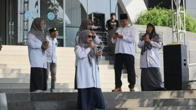 Kelompok narasumber dan panitia Lomba Vokal Dosen & Tendik Milad UMPP ke-7 berdiri khidmat di atas panggung terbuka Edutorium UMS. Di tengah, Prof. M. Din Syamsuddin (memegang mikrofon) memimpin doa, diapit oleh Rektor UMS Prof. Harun Joko Prayitno (kedua dari kiri) dan perwakilan panitia (ketiga dari kiri, memegang piala). Mereka mengenakan seragam batik hijau dan putih bermotif logo Muhammadiyah. Meja depan panggung dihiasi tanaman. Latar belakang menunjukkan tangga Edutorium dan spanduk acara.