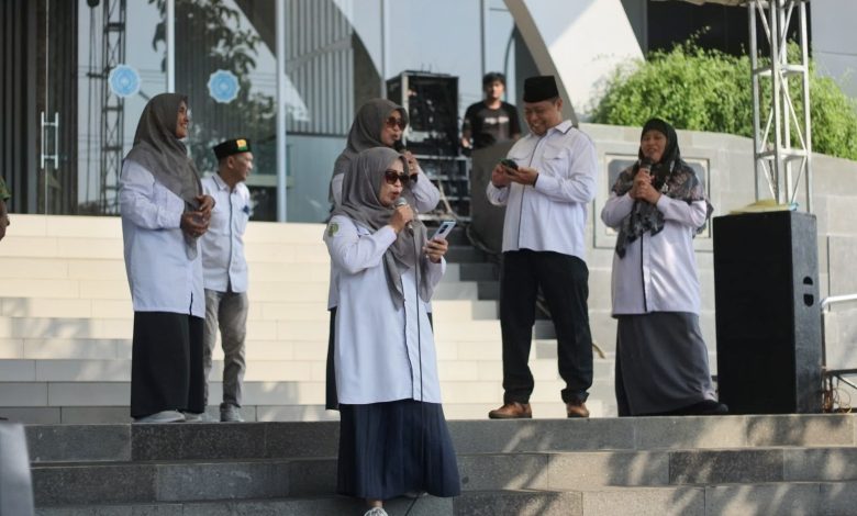 Kelompok narasumber dan panitia Lomba Vokal Dosen & Tendik Milad UMPP ke-7 berdiri khidmat di atas panggung terbuka Edutorium UMS. Di tengah, Prof. M. Din Syamsuddin (memegang mikrofon) memimpin doa, diapit oleh Rektor UMS Prof. Harun Joko Prayitno (kedua dari kiri) dan perwakilan panitia (ketiga dari kiri, memegang piala). Mereka mengenakan seragam batik hijau dan putih bermotif logo Muhammadiyah. Meja depan panggung dihiasi tanaman. Latar belakang menunjukkan tangga Edutorium dan spanduk acara.
