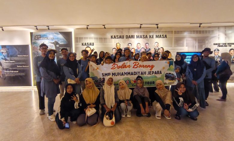 Rombongan besar siswa dan guru SMP Muhammadiyah Jepara berpose bersama di panggung terbuka Edutorium K.H. Ahmad Dahlan UMS. Mereka mengenakan seragam batik hijau dan putih berlogo Muhammadiyah, serta jilbab hijau. Di tengah, Prof. M. Din Syamsuddin memimpin doa, diapit oleh Rektor UMS Prof. Harun Joko Prayitno dan panitia yang memegang piala. Spanduk kecil di latar belakang bertuliskan 'EDUWISA JEPARA YOGYAKARTA - SMP MUHAMMADIYAH JEPARA'. Suasana panggung dihiasi tanaman dan bunga, dengan tangga Edutorium dan pepohonan hijau di latar belakang, di bawah langit biru yang cerah.