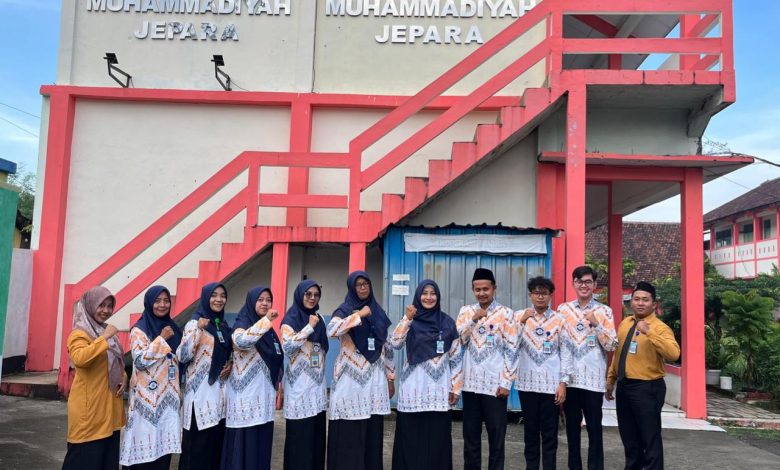 Kelompok guru SMP Muhammadiyah Jepara berpose bersama di panggung terbuka Edutorium K.H. Ahmad Dahlan UMS. Mereka mengenakan seragam batik hijau dan putih berlogo Muhammadiyah serta jilbab hijau. Di tengah, Prof. M. Din Syamsuddin memimpin doa, diapit oleh Rektor UMS Prof. Harun Joko Prayitno dan perwakilan panitia (ketiga dari kanan, memegang piala). Spanduk kecil di latar belakang bertuliskan 'HARDIKNAS SMP MUHAMMADIYAH JEPARA - PENDIDIKAN BERKEMAJUAN & BERAKHLAK MULIA'. Panggung dihiasi tanaman dan bunga. Di latar depan, ratusan siswa SD/MI Muhammadiyah/Aisyiyah, juga mengenakan pakaian ihram dan jilbab putih, duduk khidmat mengikuti doa. Latar belakang menunjukkan tangga Edutorium dan pepohonan hijau di bawah langit biru yang cerah.