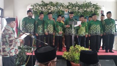 Prosesi pelantikan dan pengambilan sumpah 21 Direktur PKBM Surya Muhammadiyah Banyumas di atas panggung dengan latar belakang bunga putih, semua mengenakan seragam hijau batik dan peci.