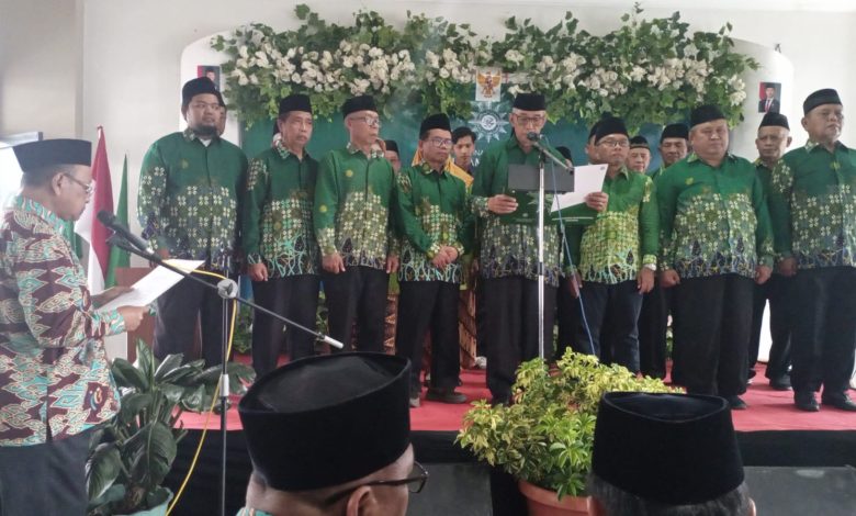 Prosesi pelantikan dan pengambilan sumpah 21 Direktur PKBM Surya Muhammadiyah Banyumas di atas panggung dengan latar belakang bunga putih, semua mengenakan seragam hijau batik dan peci.