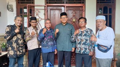Enam pria, termasuk Kyai Utsman Arif Fatkha, berpose bersama di depan pintu kayu dengan kepalan tangan, sebagai simbol sinergi antara MBS Bumiayu dan PCM Pemalang dalam kunjungan silaturrahmi.