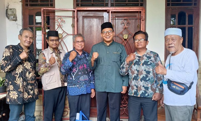 Enam pria, termasuk Kyai Utsman Arif Fatkha, berpose bersama di depan pintu kayu dengan kepalan tangan, sebagai simbol sinergi antara MBS Bumiayu dan PCM Pemalang dalam kunjungan silaturrahmi.