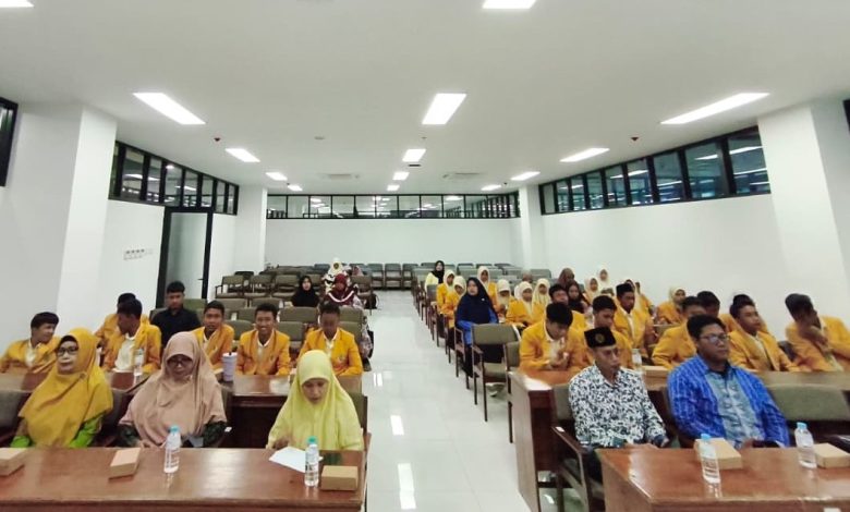 Suasana ruang rapat lantai 3 Gedung FEB UMS yang dipenuhi peserta workshop. Di baris depan duduk tiga ibu pemateri berhijab dan dua bapak pemateri berkemeja. Di belakang mereka, puluhan pelajar IPM SMP MUTU mengenakan jas almamater kuning duduk rapi menyimak acara. Ruangan terang dengan deretan lampu panel dan plafon tinggi dengan unit AC kaset sentral. Terdapat botol air mineral di setiap meja kayu.