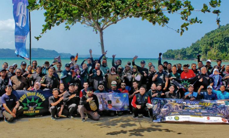 Sekelompok besar pengendara sepeda motor (bikers) berfoto bersama di pantai tropis dengan bendera BikersMu dan spanduk Kopdargab VI.