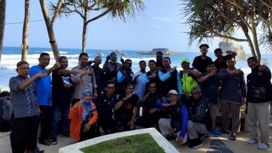 Sekelompok pengendara BikersMu berpose bersama di lokasi berpemandangan indah, seperti Pantai Buyutan, Pacitan, Jawa Timur. Mereka berdiri di bawah pohon pandan laut di sebuah pos pengamatan beton, menghadap ke laut biru yang luas dengan formasi batuan lepas pantai yang unik. Beberapa anggota membuat tanda salam khas Muhammadiyah dengan tangan mereka, melambangkan kebersamaan dan ukhuwah Islamiyah.