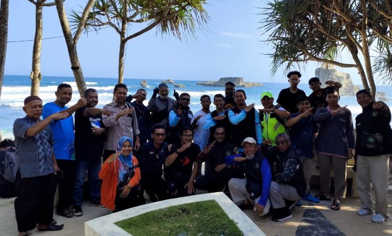 Sekelompok pengendara BikersMu berpose bersama di lokasi berpemandangan indah, seperti Pantai Buyutan, Pacitan, Jawa Timur. Mereka berdiri di bawah pohon pandan laut di sebuah pos pengamatan beton, menghadap ke laut biru yang luas dengan formasi batuan lepas pantai yang unik. Beberapa anggota membuat tanda salam khas Muhammadiyah dengan tangan mereka, melambangkan kebersamaan dan ukhuwah Islamiyah.