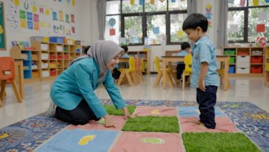 Seorang mahasiswi UMS berhijab mendampingi anak laki-laki menggunakan inovasi Karpet RABA sebagai media stimulasi anak ADHD.
