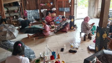 Beberapa wanita sedang melukis motif batik dan bunga pada payung tradisional di sebuah bengkel kerajinan tangan.