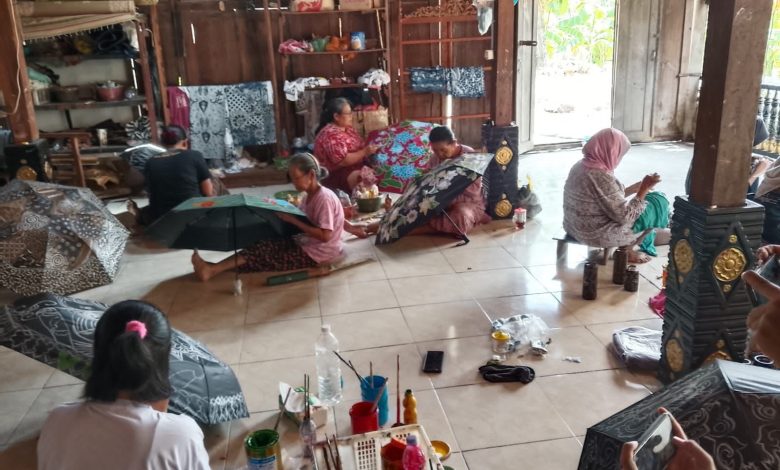 Beberapa wanita sedang melukis motif batik dan bunga pada payung tradisional di sebuah bengkel kerajinan tangan.