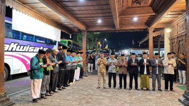 Suasana doa bersama jemaah calon haji Kabupaten Wonosobo di depan bus pemberangkatan dengan latar belakang arsitektur pendopo yang khas.