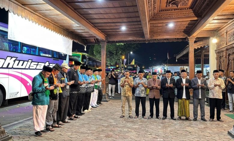 Suasana doa bersama jemaah calon haji Kabupaten Wonosobo di depan bus pemberangkatan dengan latar belakang arsitektur pendopo yang khas.