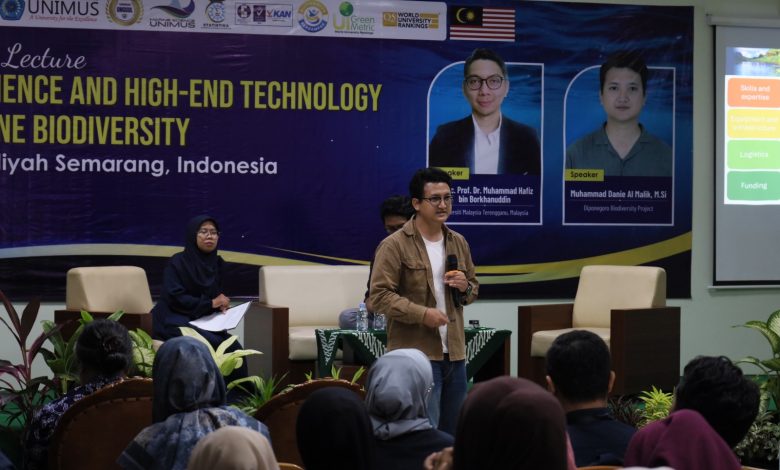 Seorang pembicara pria di atas panggung memberikan presentasi tentang teknologi eDNA untuk konservasi laut dalam sebuah kuliah umum internasional di UNIMUS Semarang. Latar belakang menunjukkan spanduk acara.