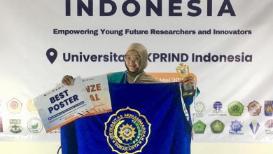 Mahasiswi UMS pemenang penghargaan Olimpiade Penelitian Indonesia 2026 membentangkan bendera Universitas Muhammadiyah Surakarta sambil memegang trofi dan piagam penghargaan.