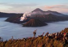 Pemandangan matahari terbit di Gunung Bromo dengan lautan awan menutupi kawah Batok dan Bromo, serta wisatawan berkumpul di bukit penanjakan, di latar belakang terlihat Gunung Semeru.