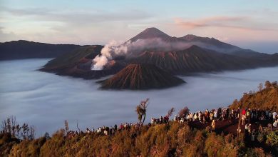 Pemandangan matahari terbit di Gunung Bromo dengan lautan awan menutupi kawah Batok dan Bromo, serta wisatawan berkumpul di bukit penanjakan, di latar belakang terlihat Gunung Semeru.