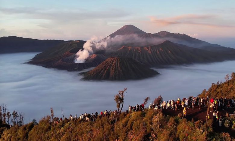 Pemandangan matahari terbit di Gunung Bromo dengan lautan awan menutupi kawah Batok dan Bromo, serta wisatawan berkumpul di bukit penanjakan, di latar belakang terlihat Gunung Semeru.