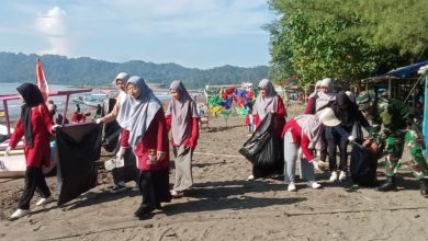 Sekelompok perempuan berjilbab dengan seragam Nasyiatul Aisyiyah Cilacap berjalan beriringan di Pantai Teluk Penyu, membawa kantong sampah hitam besar. Tampak pula seorang anggota TNI membantu mereka. Di latar belakang, terlihat perahu nelayan, laut, dan bukit hijau.