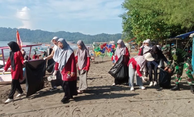 Sekelompok perempuan berjilbab dengan seragam Nasyiatul Aisyiyah Cilacap berjalan beriringan di Pantai Teluk Penyu, membawa kantong sampah hitam besar. Tampak pula seorang anggota TNI membantu mereka. Di latar belakang, terlihat perahu nelayan, laut, dan bukit hijau.