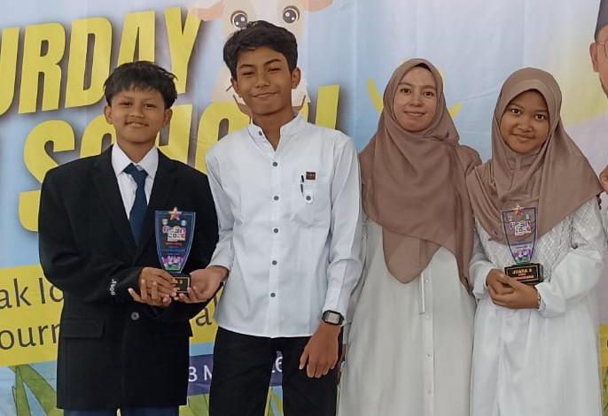 Tiga siswa SMP Mutual Magelang berprestasi, Reyhan Aldre, Seto Ayodhya, dan Khanza Kineta Asmarani, berdiri bangga bersama seorang guru perempuan berhijab, usai menerima piala juara di ajang FLS2N 2026 Kota Magelang. Siswa laki-laki di kiri memegang piala, sementara siswi di kanan memegang pialanya yang tertulis 'JUARA 3'. Background panggung memiliki tulisan 'SATURDAY SCHOOL' dan ilustrasi gajah yang ceria.