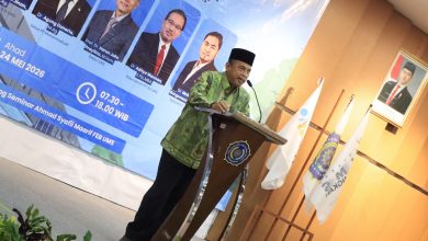 Foto Dr. H. Agung Danarto, M.Ag. berbaju batik hijau dan peci hitam sedang memberikan pemaparan materi Stadium Generale IKA UMS dari atas podium, berlatar spanduk biru acara Rakernas IV di Gedung FEB UMS.