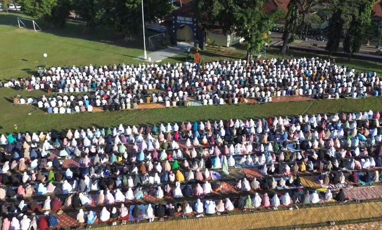 Foto udara ribuan jamaah mengenakan pakaian putih dan mukena warna-warni sedang duduk khusyuk mengikuti pelaksanaan Salat Iduladha 2026 di lapangan Alun-Alun Kutoarjo yang dikelilingi pepohonan.