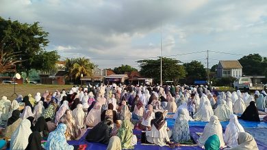 Ribuan jamaah wanita mengenakan mukena putih sedang duduk khusyuk mengikuti Sholat Idul Adha 2026 Jepara di Alun-Alun Kelet yang berlatar pemukiman warga di bawah langit berawan.