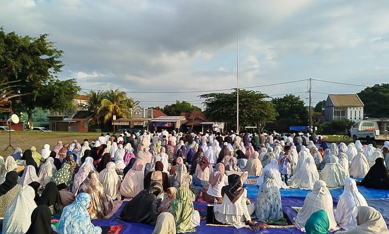 Ribuan jamaah wanita mengenakan mukena putih sedang duduk khusyuk mengikuti Sholat Idul Adha 2026 Jepara di Alun-Alun Kelet yang berlatar pemukiman warga di bawah langit berawan.