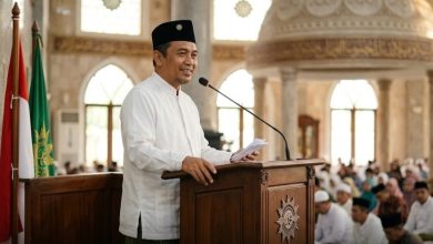 Ilustrasi seorang khatib pria berbaju koko putih dan peci hitam sedang menyampaikan khutbah Idul Adha di atas mimbar masjid di hadapan jamaah.