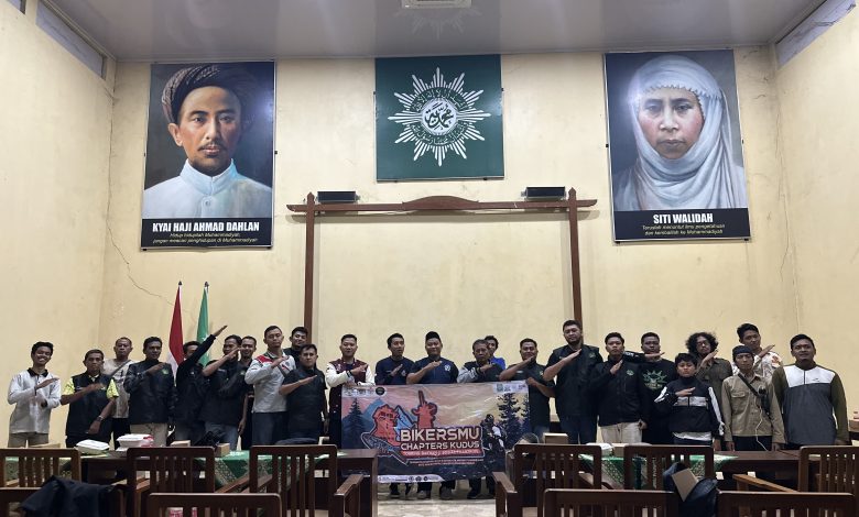 Anggota BikersMu Muria Raya berfoto bersama membentangkan spanduk di dalam ruangan aula berlatar belakang foto K.H. Ahmad Dahlan dan Siti Walidah.