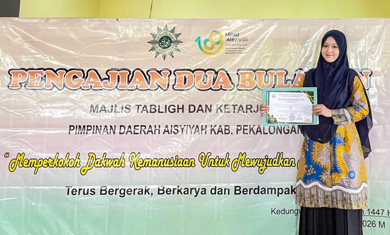 Nagita Histimuna Aisyah memegang piagam penghargaan Juara 1 lomba video kultum di depan spanduk Majelis Tabligh dan Ketarjihan Aisyiyah Kabupaten Pekalongan.