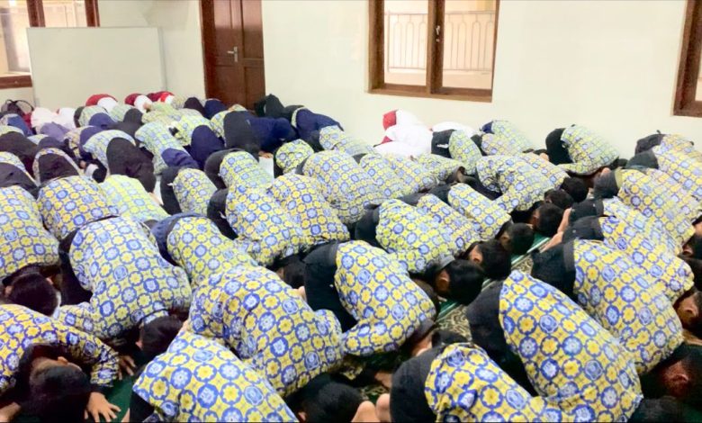 Puluhan siswa SD Muhammadiyah PK Banyudono dalam seragam batik biru-kuning melakukan sujud syukur massal di Masjid Asyiroj. Punggung mereka memenuhi karpet hijau, menciptakan pola mosaik visual yang mengharukan.